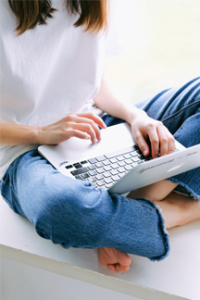 barefoot student in jeans and white tee shirt uses laptop