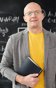 teacher in yellow shirt and gray blazer holds notebook in classroom